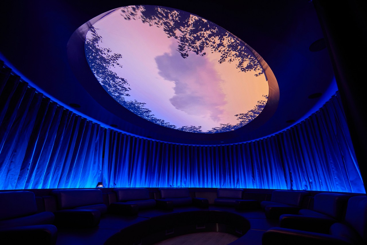 Forest Meditation room lined with comfortable seating and a glass dome on the ceiling to observe the sky lined with tree branches.